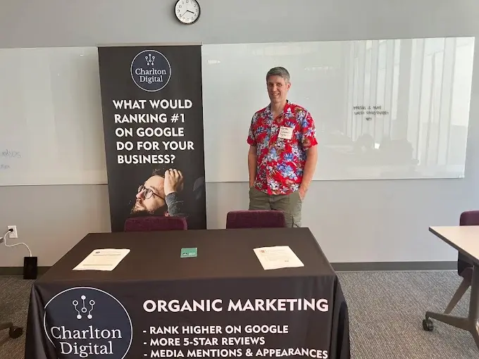 Aaron Charlton standing beside Charlton Digital banners and a display table at a business event
